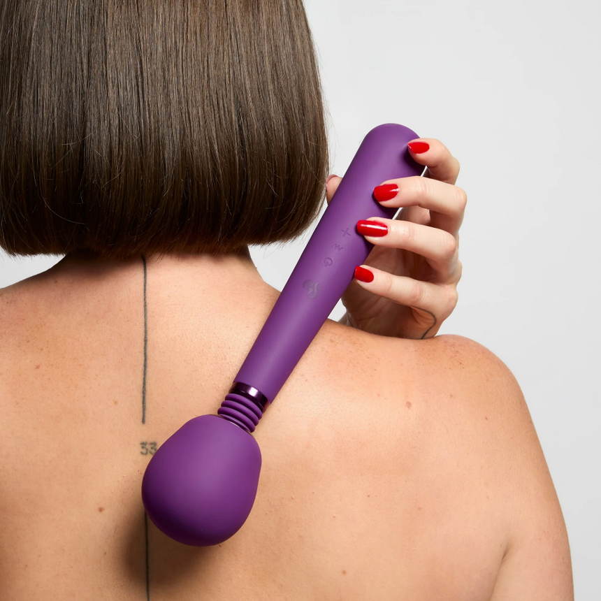 Woman holding So Divine Rechargeable Couple's Wonder Wand Purple against her back in a white studio setting.