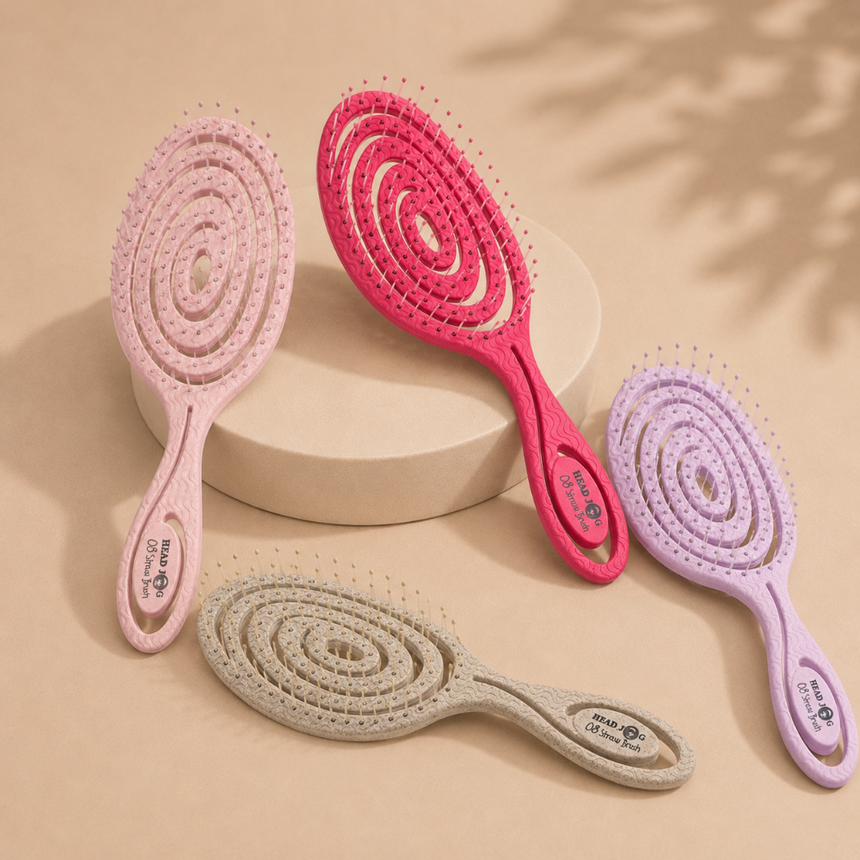 Head Jog detangling hairbrushes in lilac, light pink, hot pink and beige displayed on a neutral beige background.