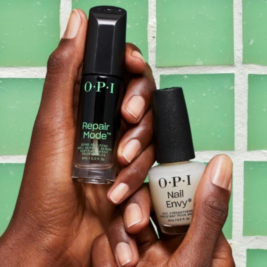 Hands holding OPI Repair Mode and Nail Envy nail treatments against a green tiled background.