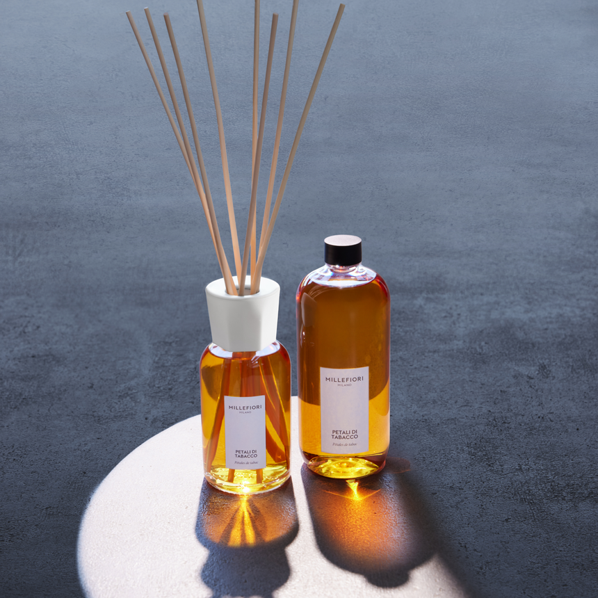 Millefiori Petali di Tabacco reed diffuser and refill bottle displayed in warm sunlight against a dark textured backdrop.