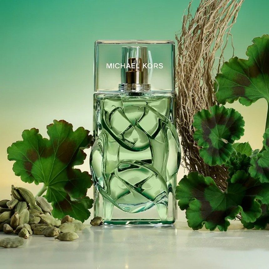 Michael Kors fragrance bottle surrounded by green leaves and cardamom pods.
