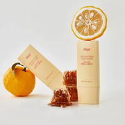 House Of Hur Weightless Sun Fluid surrounded by fresh fruit and honey on a clean white studio backdrop.