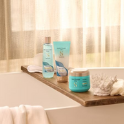 Sanctuary Spa body care products displayed on a wooden bath tray beside a sunlit bathtub.