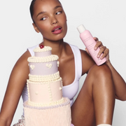 Model holding a Gem Deodorant product beside a pastel tiered celebration cake against a light studio backdrop.
