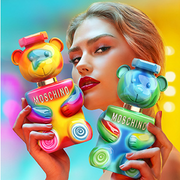 Model holding two colourful Moschino Toy 2 Bubble Gum fragrance bottles against a vibrant multicoloured background.

