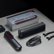 Tymo Porta Pro heated styling brush with storage case, charging cable and hair clips displayed on a dark studio surface.