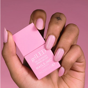 Hand holding Nails Inc. Gel LED Polish against a pink backdrop.