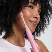 Woman holding a pink Ordo Electric Toothbrush against a white backdrop.