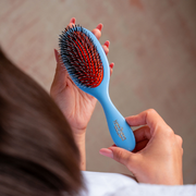 Woman holding Mason Pearson Pocket Bristle & Nylon Hairbrush Blue against a blurred backdrop.