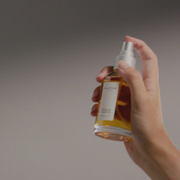 Millefiori home fragrance spray held in hand against a soft neutral grey backdrop.