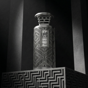 Silver Arabic fragrance bottle with intricate geometric detailing, displayed on a patterned pedestal against a dramatic black background.