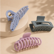 Head Jog claw hair clips in lilac, grey and pink, displayed on a neutral beige background.