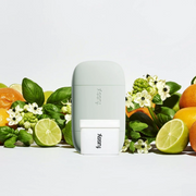 Fussy deodorant and refill displayed with fresh citrus fruits, green leaves and white flowers against a clean white backdrop.
