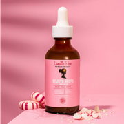 Camille Rose Rejuva Drops Hair & Scalp Oil displayed with peppermint sweets against a pink backdrop.