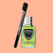 Marvis Spearmint Mouthwash Concentrate displayed with a black toothbrush against a soft peach background.

