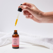 Hand using a dropper with Sukin Certified Organic Rose Hip Oil against a soft white backdrop.
