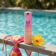 2BTanned Carrot Oil displayed beside a yellow hibiscus flower and bikini top against a sunlit swimming pool backdrop.
