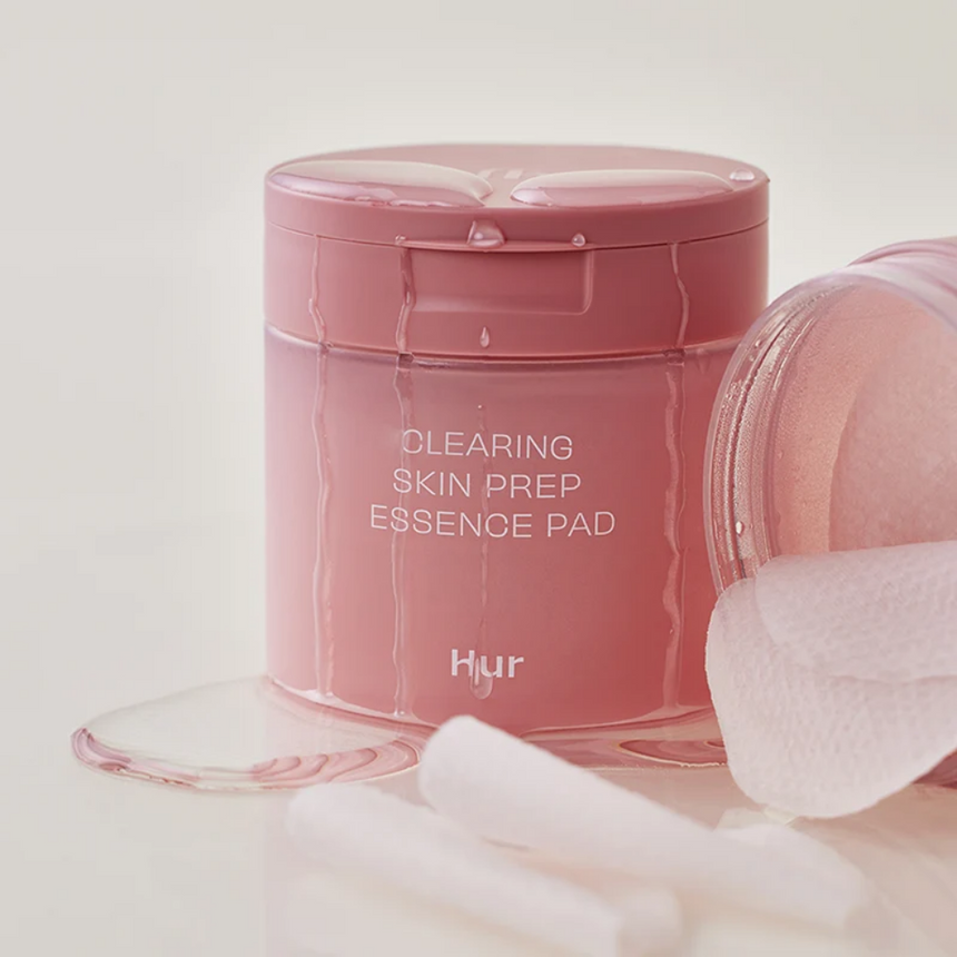 House Of Hur Clearing Skin Prep Essence Pad with water droplets, displayed against a soft light neutral studio backdrop.