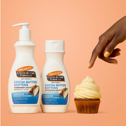 Palmer’s Cocoa Butter Softeners body lotion displayed with a frosted cupcake against a warm peach background.