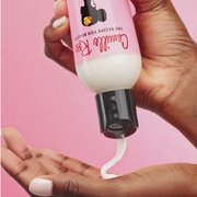 Hand dispensing Camille Rose Naturals Curl Love Moisture Milk against a soft pink backdrop
