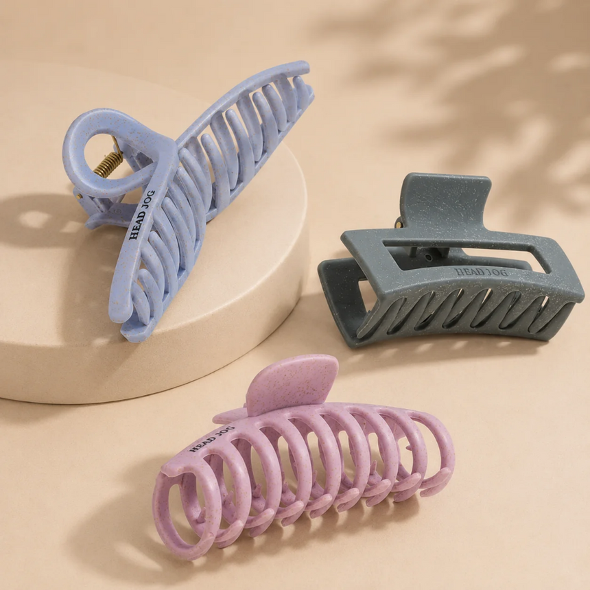 Head Jog claw hair clips in lilac, grey and pink, displayed on a neutral beige background.