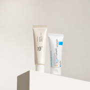 Beauty of Joseon Relief Sun Rice + Probiotics SPF50+ and La Roche-Posay Cicaplast Baume B5+ SPF50 displayed on a white plinth against a soft neutral backdrop.
