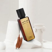 Zimaya Ihmam Al Oud fragrance bottle with a gold label and black cap, displayed among white classical columns and warm oud wood.