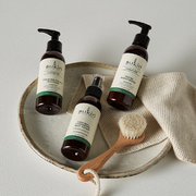 Sukin Skincare products displayed with a cleansing brush and textured cloth on a ceramic tray.