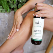Woman applying Sukin Signature Hydrating Body Lotion against a bathroom-inspired backdrop.