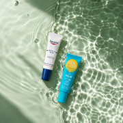 Eucerin Acute Lip Balm and Bondi Sands SPF 50+ Lip Balm displayed on a rippling green water surface with sunlight reflections.