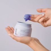 Hands holding a Schwarzkopf Professional bond Repair Purple Mask jar, with a small amount of product scooped onto a fingertip.
