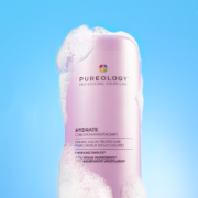 Pureology Hydrate Conditioner bottle displayed with foamy product texture against a bright blue background.