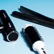 Hair styling tools including a hairdryer, straighteners and round brush displayed against a light blue background.