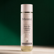 Miniml Non-Bio Laundry Liquid bottle displayed upright on a cream surface against a deep green background.