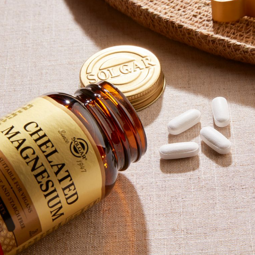 Solgar Chelated Magnesium supplement bottle displayed with capsules and its gold lid against a softly lit neutral backdrop.
