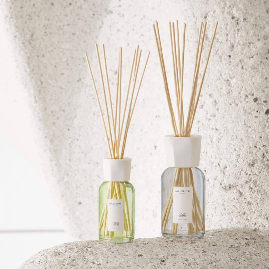Millefiori reed diffusers displayed on a textured stone surface against a light neutral backdrop.