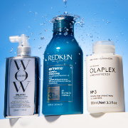 Color Wow, Redken and Olaplex haircare products displayed with splashing water against a light blue background.