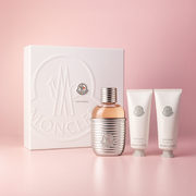 Moncler Pour Femme women’s fragrance gift set with eau de parfum and body care products displayed on a soft pink background.