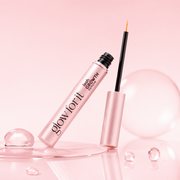 Glow For It Lash Growth Serum displayed against a glossy pink backdrop with clear, bubble-like textures.